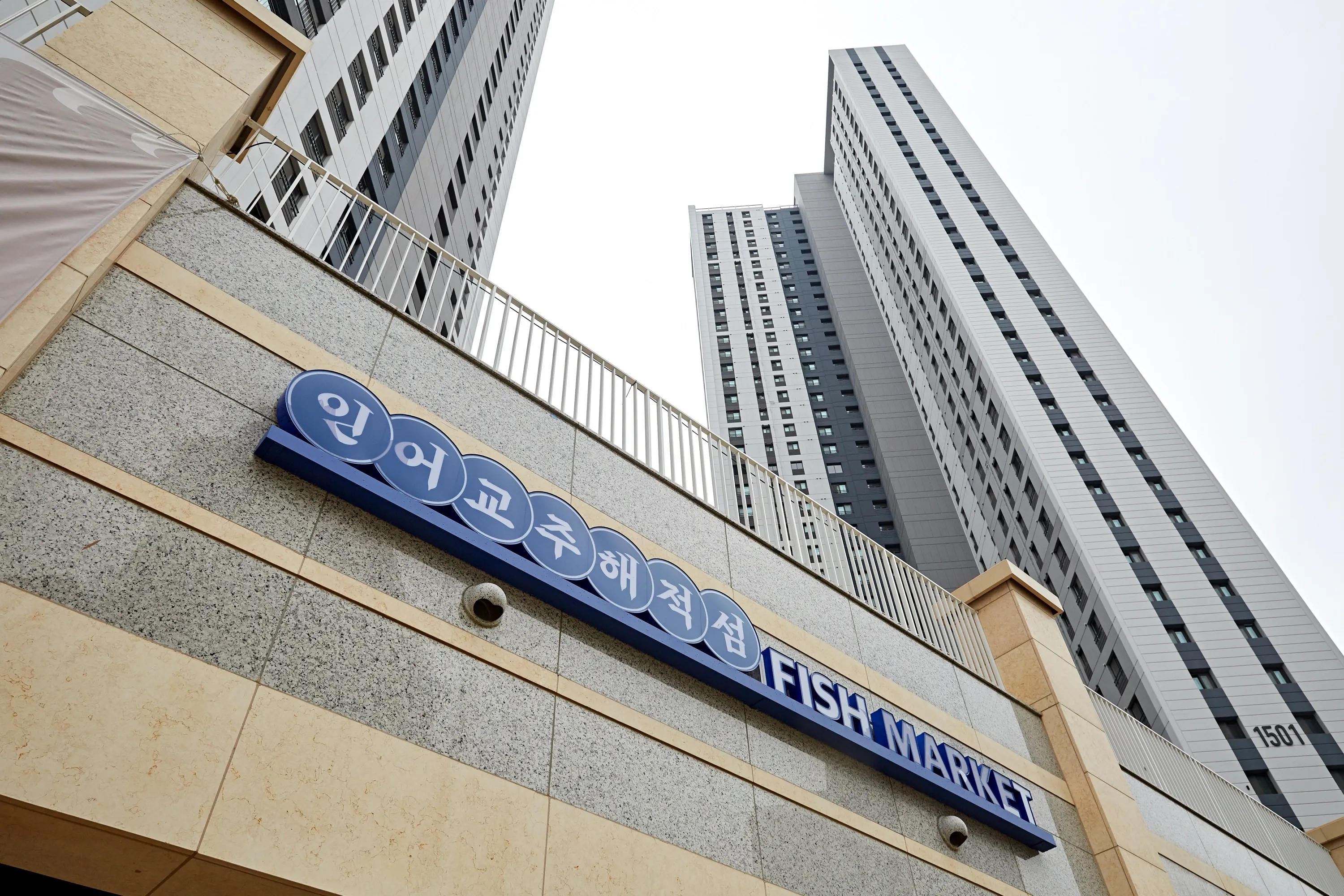 인어교주해적섬 다이닝 회색 대리석 벽과 베이지 테두리 파란 간판 뒤로 솟은 고층 아파트