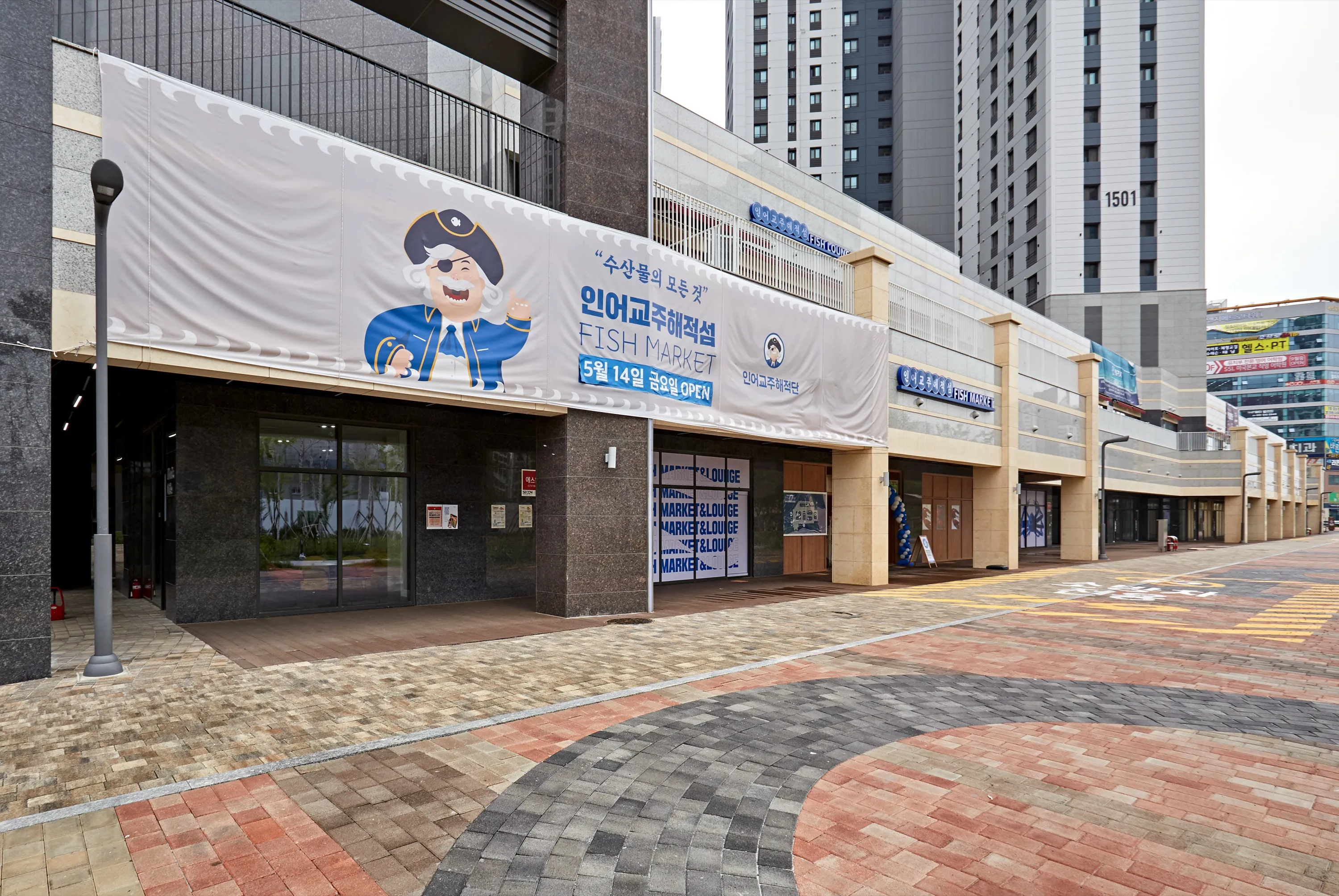 인어교주해적섬 다이닝 검은 대리석 외벽 통유리 매장 위 해적 캐릭터 현수막과 벽돌 보도